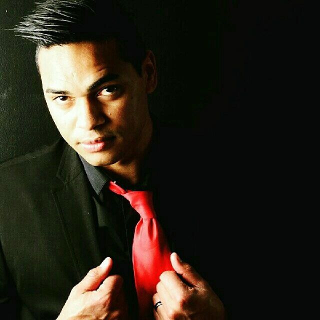 CLOSE-UP PORTRAIT OF MATURE MAN WITH HAND ON BLACK BACKGROUND