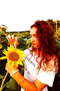 Beautiful young woman standing by flowering plants against sky