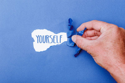 Close-up of hand holding text against blue wall