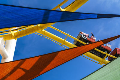 Color flags closeup with roller coaster in background, against blue sky. 