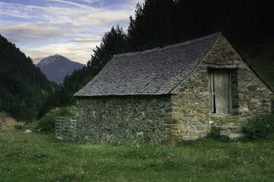 Old house on field by mountain against sky