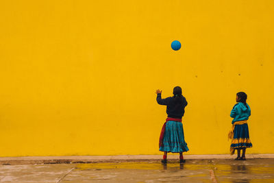 Rear view of girls playing with ball against yellow wall