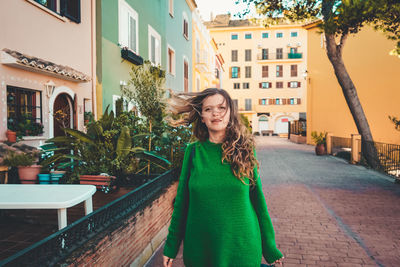 Portrait of smiling young woman standing against buildings