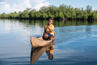 Portrait of smiling young woman sitting on lake against trees