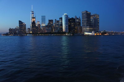 Illuminated buildings by sea against sky in city