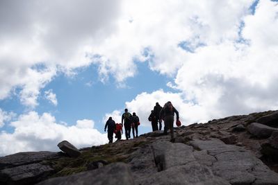 Low angle view of people on rocks against sky