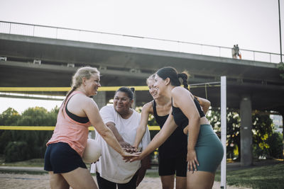 Smiling female friends stacking hands while playing volleyball