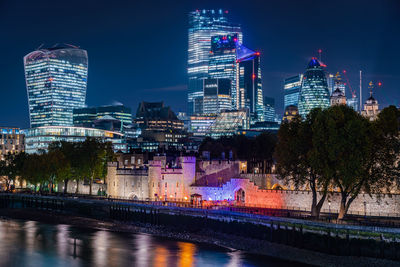 Illuminated buildings by river against sky at night