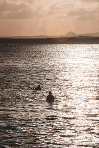 Silhouette swimming in sea against sky during sunset