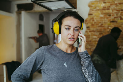 Female construction manager wearing ear protectors talking through smart phone at site