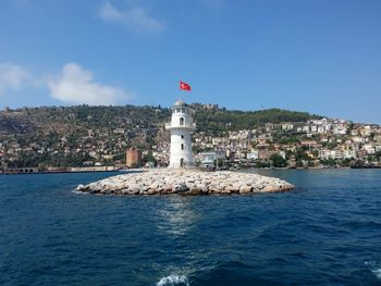 Lighthouse amidst buildings and sea against sky