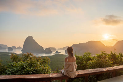 Rear view of woman sitting on mountain against sky during sunset