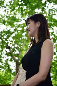 Young woman looking away while standing against trees