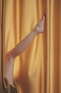 Low section of woman touching yellow window curtains