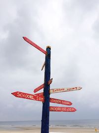 Close-up of directional sign on beach against sky