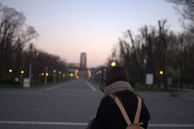 Rear view of woman in city against sky during sunset