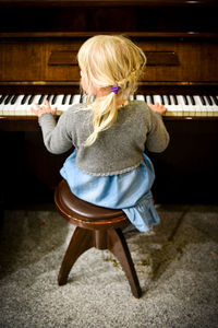 Rear view of girl playing piano at home