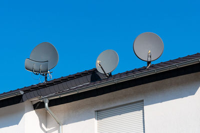 Three satellite dishes on the roof of a tiled house. clear blue sky.