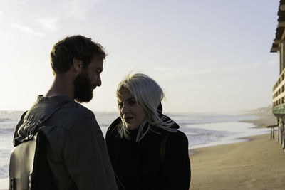 Young couple standing on beach against sky