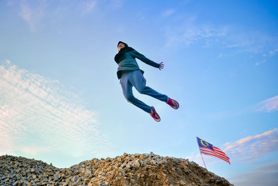 Low angle view of girl jumping by flag against sky