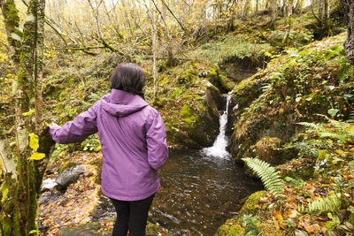 Rear view of woman standing by stream in forest