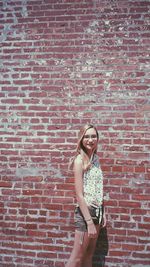 Portrait of smiling young woman standing against brick wall