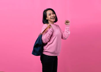 Young woman standing against pink background