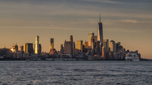 Sea by buildings against sky during sunset