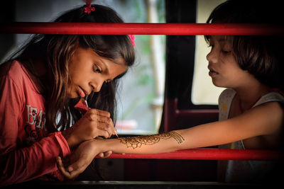 Girl applying henna tattoo on sister forearm
