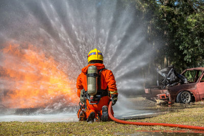 Rear view of firefighter spraying water on field