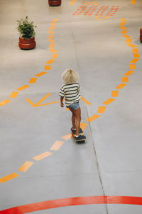 Blond woman skateboarding on footpath with orange road marking