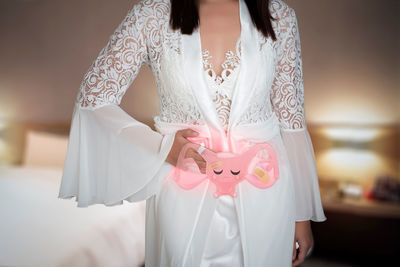 Midsection of woman standing against white curtain at home