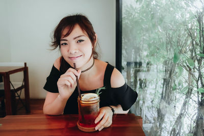 Portrait of smiling woman with drink sitting at restaurant