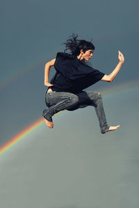 Full length of young woman jumping against clear sky