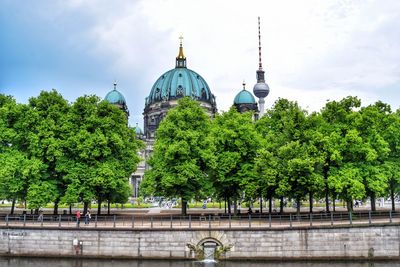 Berlin cathedral and fernsehturm tower in front of trees and river against sky