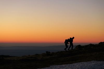 Silhouette friends walking on mountain against sky during sunset