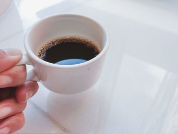 Close-up of hand holding coffee cup on table