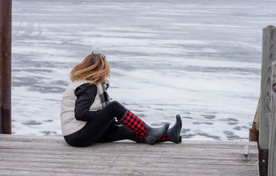 Full length of woman sitting on wood during winter