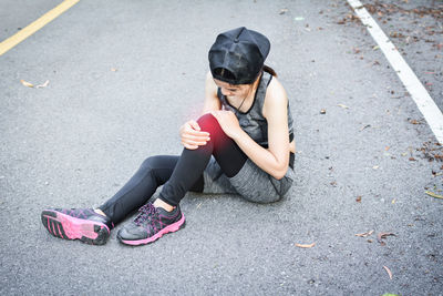 High angle view of woman wearing sports clothing with knee pain sitting on road