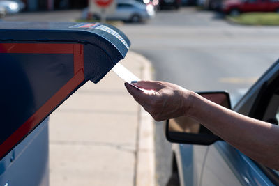 Cropped hand of woman inserting letter in mailbox through car window