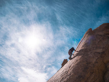 Low angle view of man climbing cliff against sky