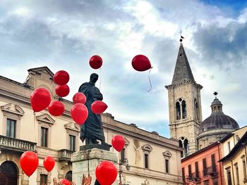 Low angle view of red balloons against cloudy sky