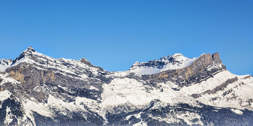 Low angle view of snowcapped mountains against clear blue sky