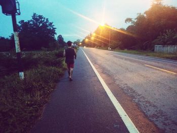 Rear view of man walking on road against sky during sunset