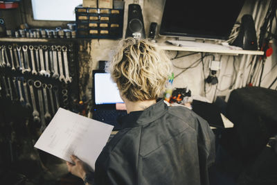 Rear view of female customer holding bill at auto repair shop