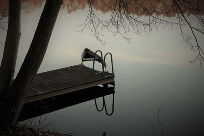 Silhouette tree by lake against sky at sunset