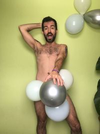 Portrait of young man with balloons against wall