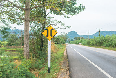 Road sign by trees against sky
