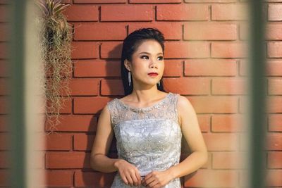 Beautiful young woman standing against brick wall seen through window