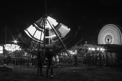 People at illuminated amusement park against sky at night